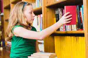 Foto gratuita ragazza che mette libro rosso sullo scaffale