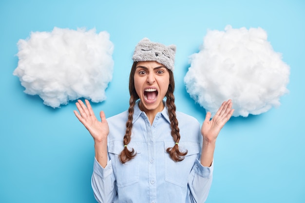 Free photo girl raises palms and exclaims loudly from anger has two combed pigtails wears soft sleepmask shirt isolated on blue