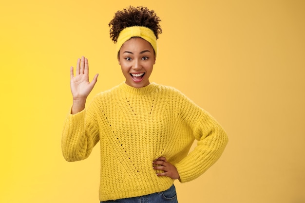 Girl raising hand gladly willing participate be candidate say hi hello waving palm greeting gesture smiling broadly feel happy gladly welcoming friends inviting party near door yellow background.