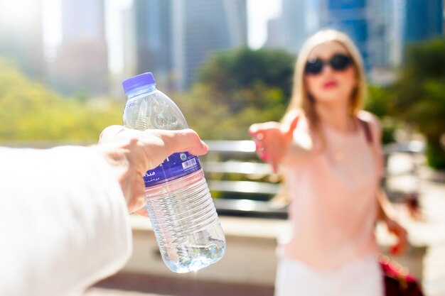 Девушка протягивает руку, чтобы взять с руки человека бутылку воды