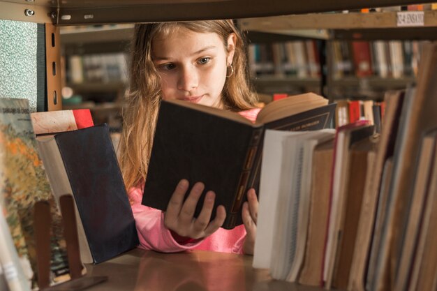Girl reading book behind bookshelf