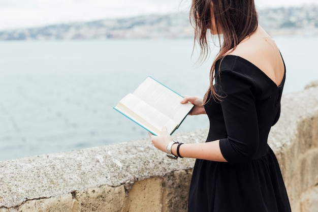 Foto gratuita ragazza che legge un libro vicino al mare