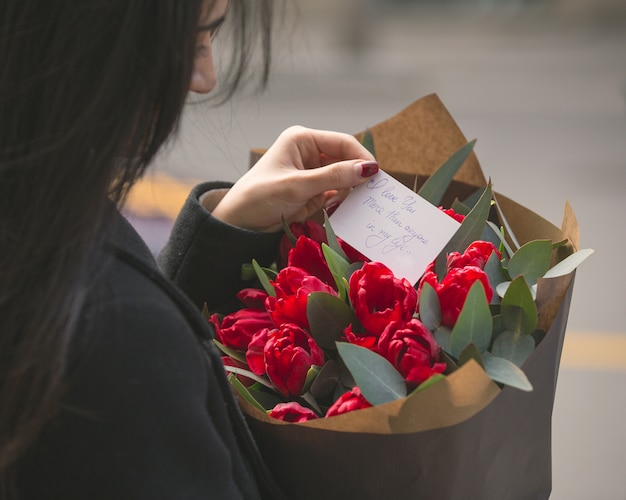 빨간 튤립 꽃다발에 넣어 메모를 읽는 여자