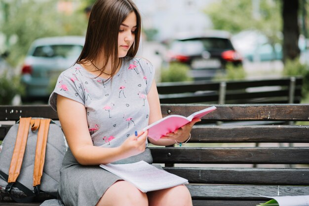 Girl reading notebook on bench