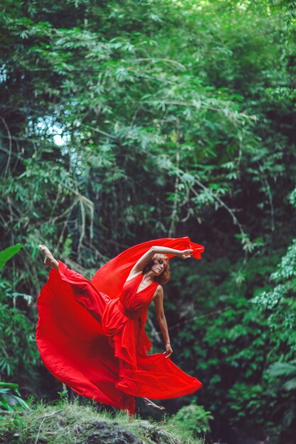 Girl in a red dress dancing in a waterfall. 