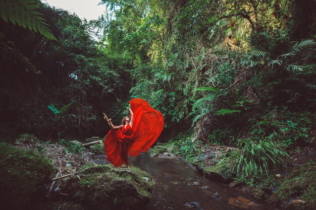 Девушка в красном платье танцует в водопаде.
