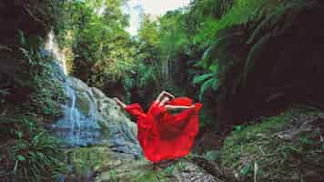 Foto gratuita ragazza in un vestito rosso che balla in una cascata.