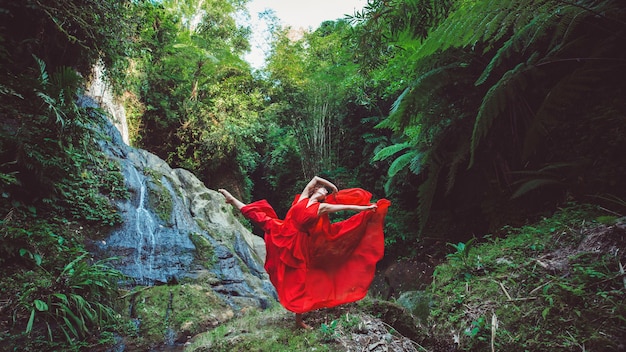 Girl in a red dress dancing in a waterfall. 