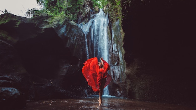 Girl in a red dress dancing in a waterfall. 