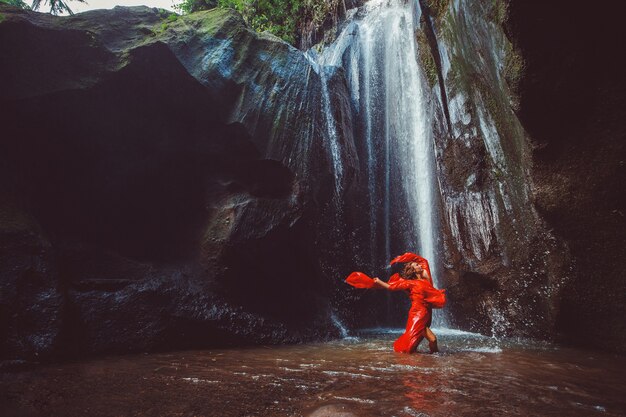 滝で踊る赤いドレスを着た女の子。