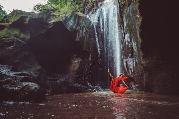 Girl in a red dress dancing in a waterfall. 