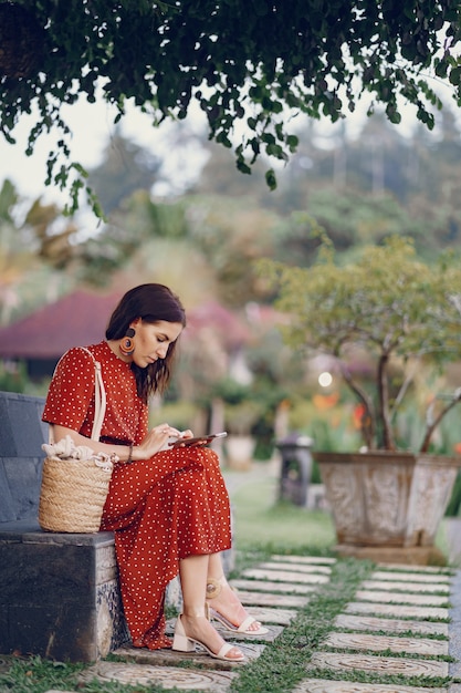 Foto gratuita la ragazza in un vestito rosso che si siede e usa il telefono