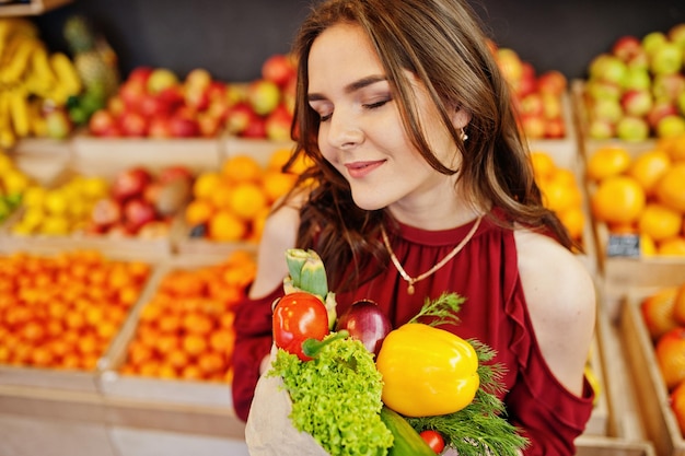 Ragazza in rosso che tiene diverse verdure sul negozio di frutta