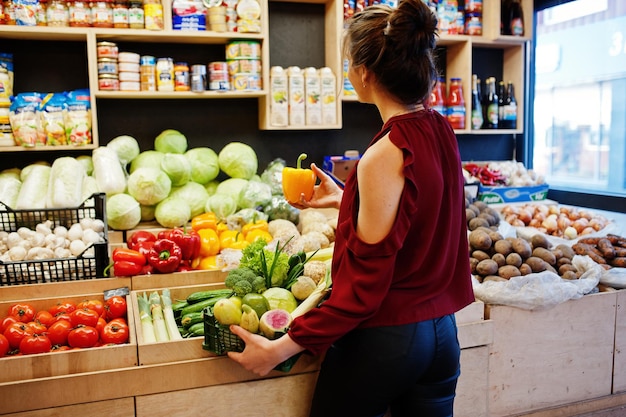 Девушка в красном держит разные овощи в магазине фруктов