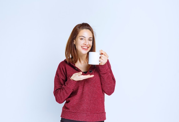 Girl in red jacket holding a white coffee mug and smelling the product.