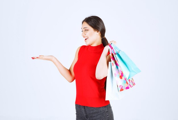 Girl in red shirt carrying colorful shopping bags behind her shoulder.