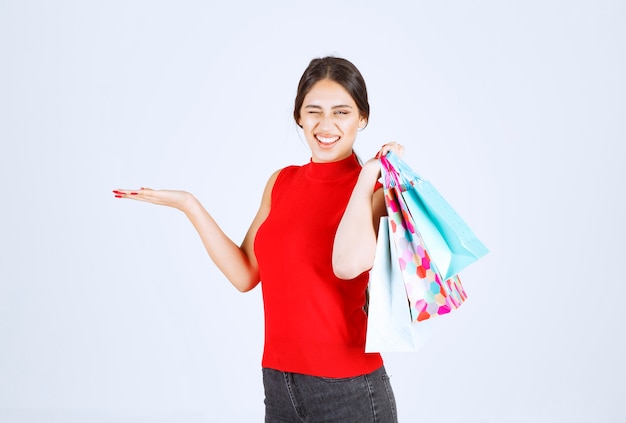 Girl in red shirt carrying colorful shopping bags behind her shoulder.