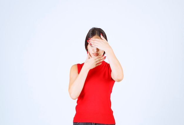 Free photo girl in red shirt covering part of her face with hand.
