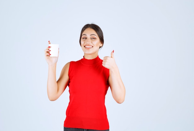 Girl in red shirt having coffee and showing positive sign.