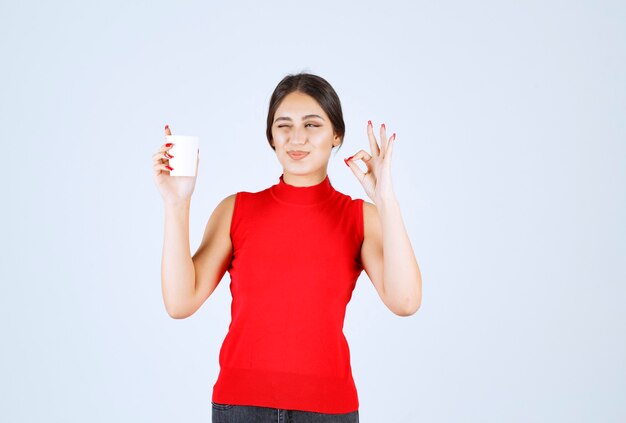 Girl in red shirt having coffee and showing positive sign.