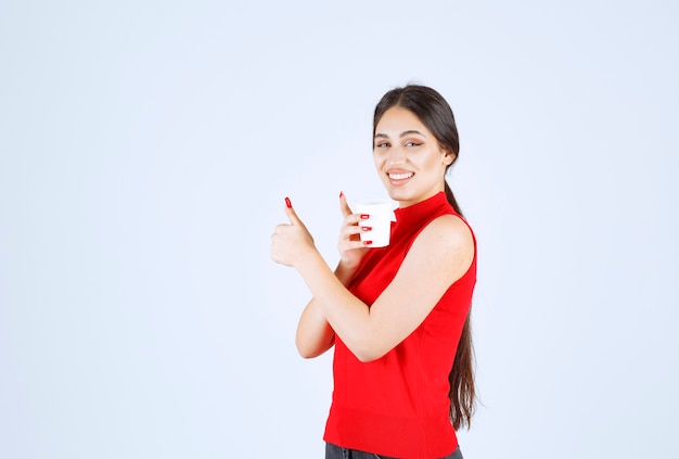 Girl in red shirt having coffee and showing positive sign.