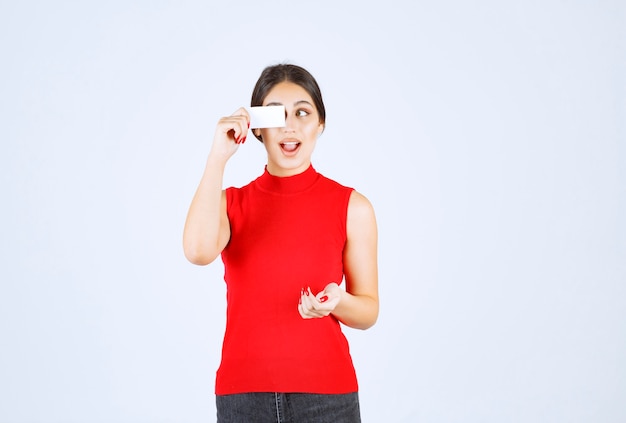 Girl in red shirt holding a business card and looks surprized.