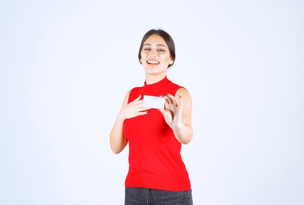 Ragazza in camicia rossa che tiene un biglietto da visita e che si presenta.