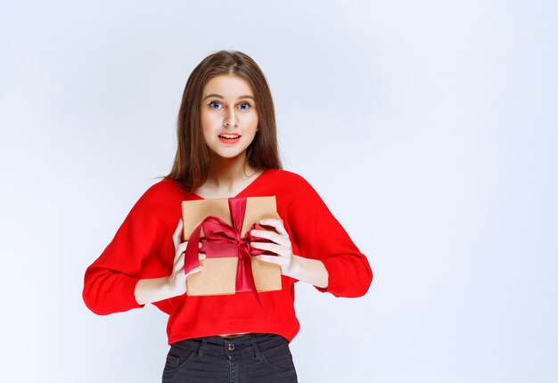 Girl in red shirt holding a cardboard gift box wrapped with red ribbon. 