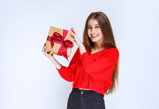 Girl in red shirt holding a cardboard gift box wrapped with red ribbon. 