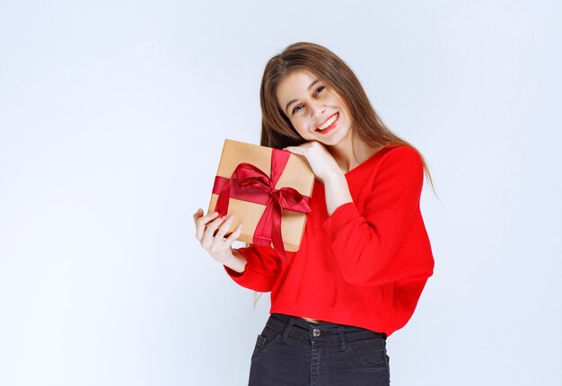 Девушка в красной рубашке держит картонную подарочную коробку, обернутую красной лентой.