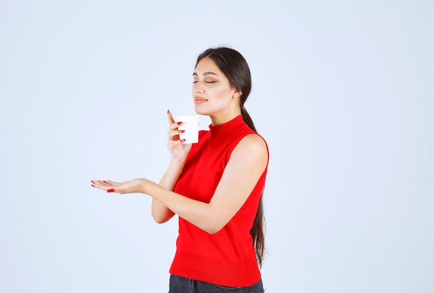 Girl in red shirt holding a coffee cup and smelling.