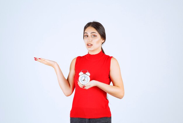 Girl in red shirt holding and promoting an alarm clock.