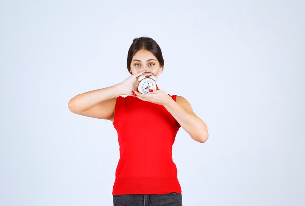 Girl in red shirt holding and promoting an alarm clock.