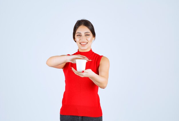 Girl in a red shirt holding a white coffee cup between hands.