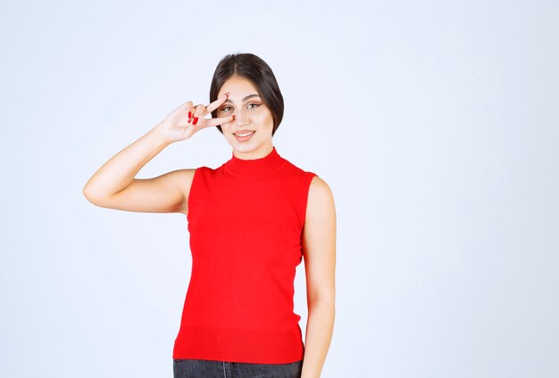 Girl in red shirt looking through her fingers.