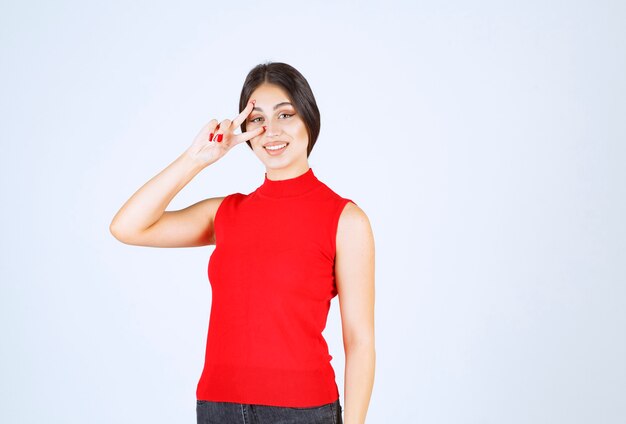 Girl in red shirt looking through her fingers.