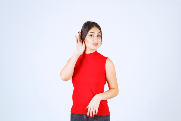 Girl in red shirt pointing her ear to hear well.