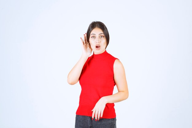 Girl in red shirt pointing her ear to hear well.