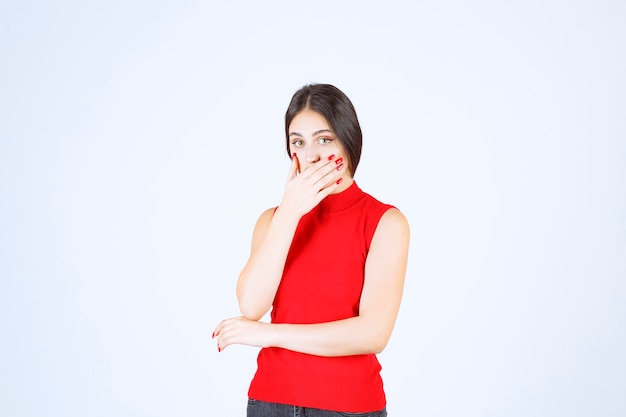 Girl in red shirt pointing at her mouth and asking for silence.