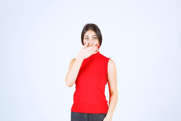 Ragazza in camicia rossa che indica la sua bocca e chiede silenzio.