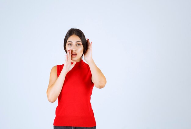 Girl in red shirt pointing at her mouth and asking for silence.