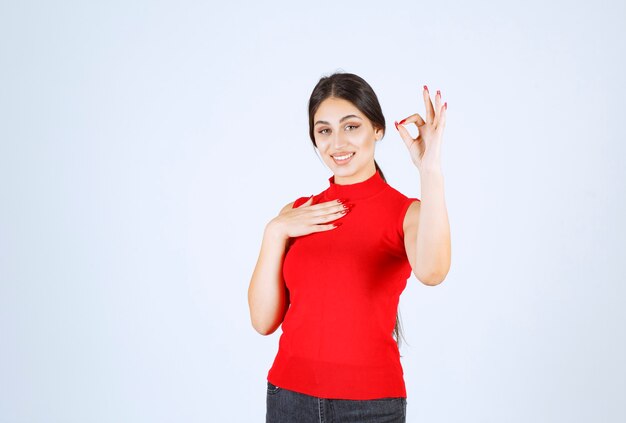 Girl in red shirt pointing at herself .