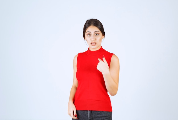 Girl in red shirt pointing at herself .