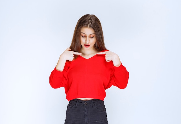 Girl in red shirt pointing at herself. 