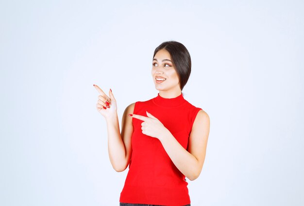 Girl in a red shirt pointing to the left side.