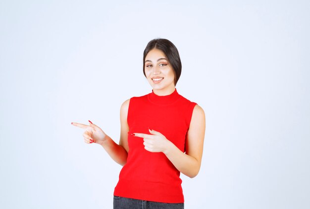 Girl in red shirt pointing at something on the left.