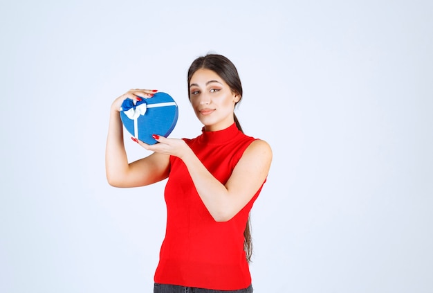 그녀의 푸른 심장 모양 선물 상자를 제시하는 빨간 셔츠에있는 여자.