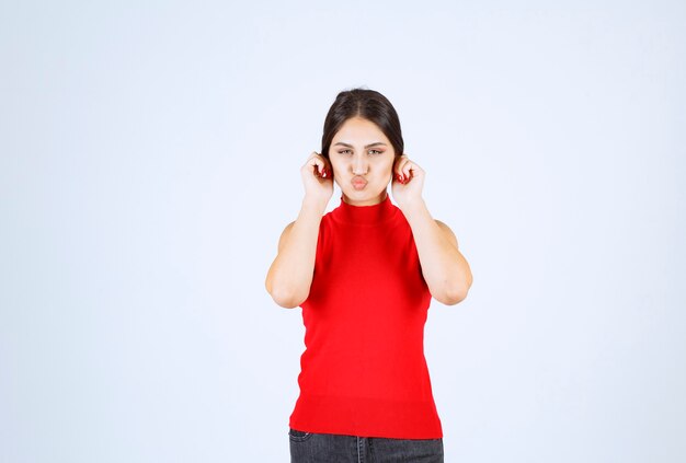 Girl in a red shirt pulling her ears as a sign of bad luck.