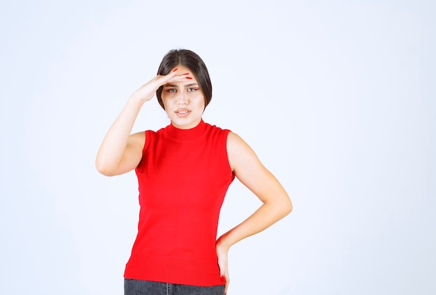 Girl in red shirt putting hand to her forehead and looking forward.