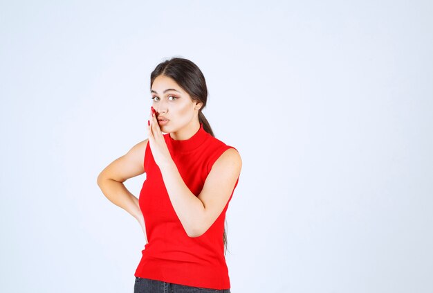 Girl in red shirt putting hand to her mouth and whispering.